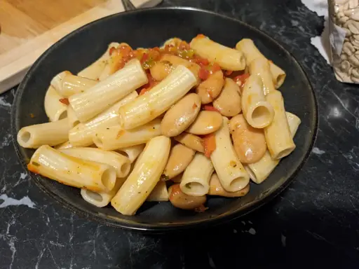 A vegan meal of rigatoni pasta, beans, and diced peppers all served in a bowl.